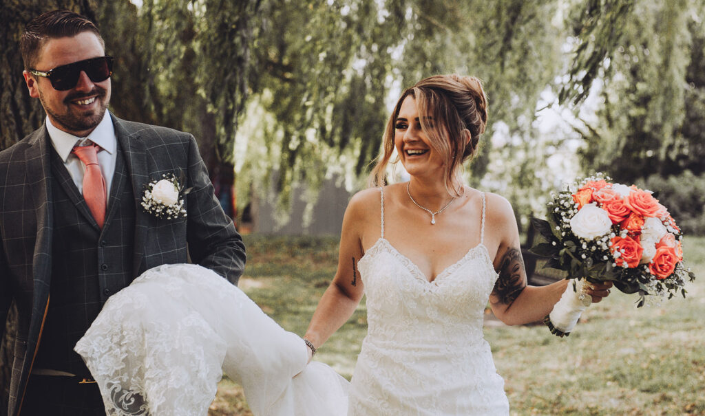 Bride and groom laughing under willow trees on the quay at their summer wedding in Sandwich, Kent.