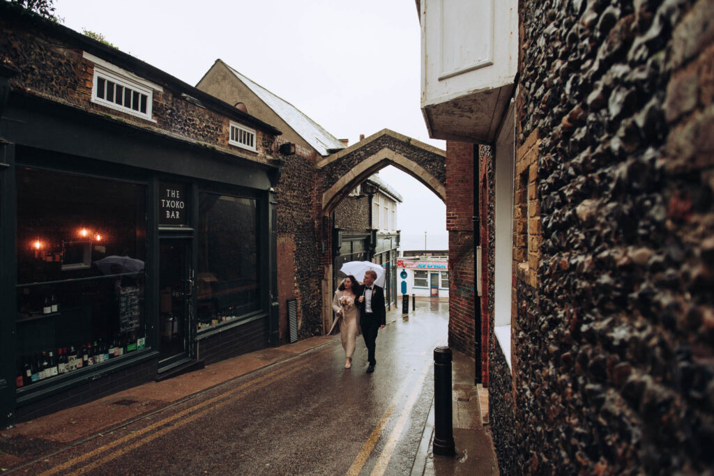 Bride and groom walking outside the txoko bar holding umbrellas in Broadstairs