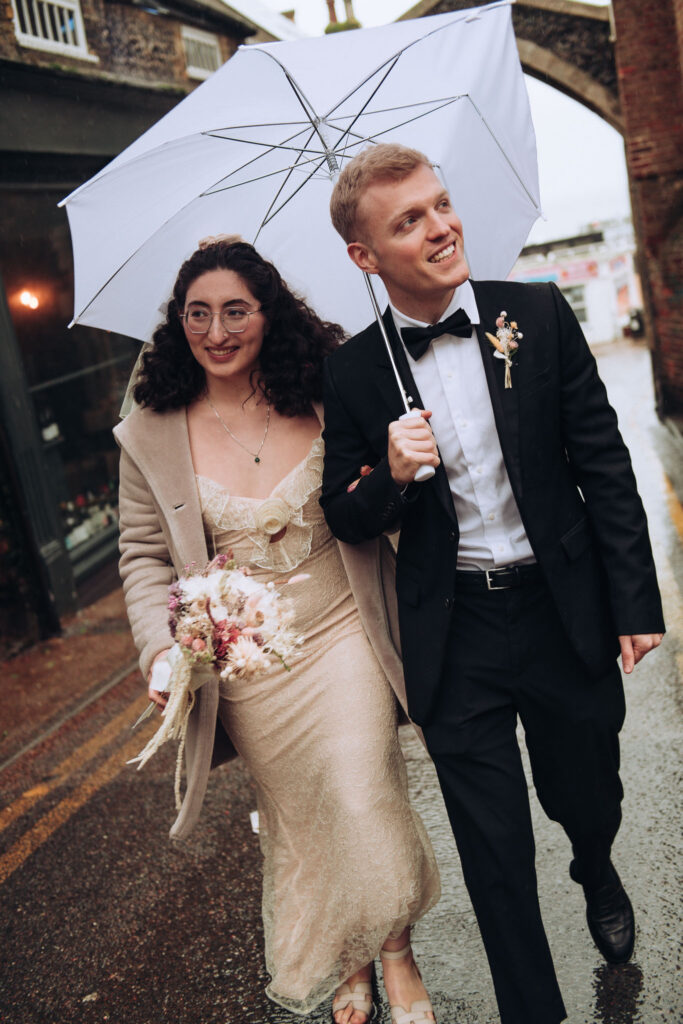 Bride and groom walking outside holding umbrellas in the rain in Broadstairs