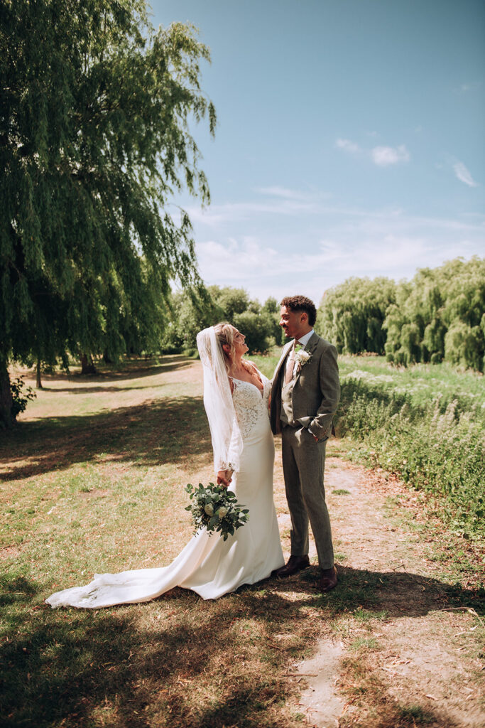 Bride and groom smiling beside willow trees in Ramsgate