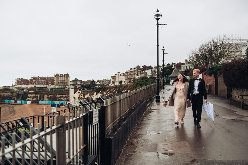 Bride and groom walking in the wind in Broadstairs beside Viking Bay