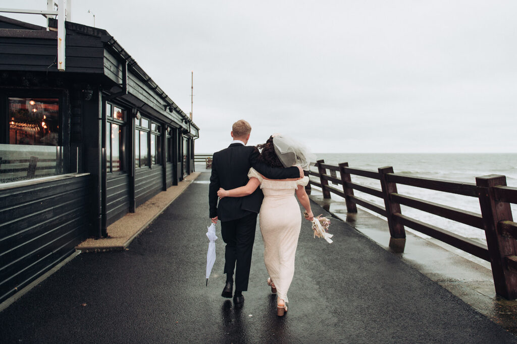 Bride and groom arm in arm walking on Viking Bay pier