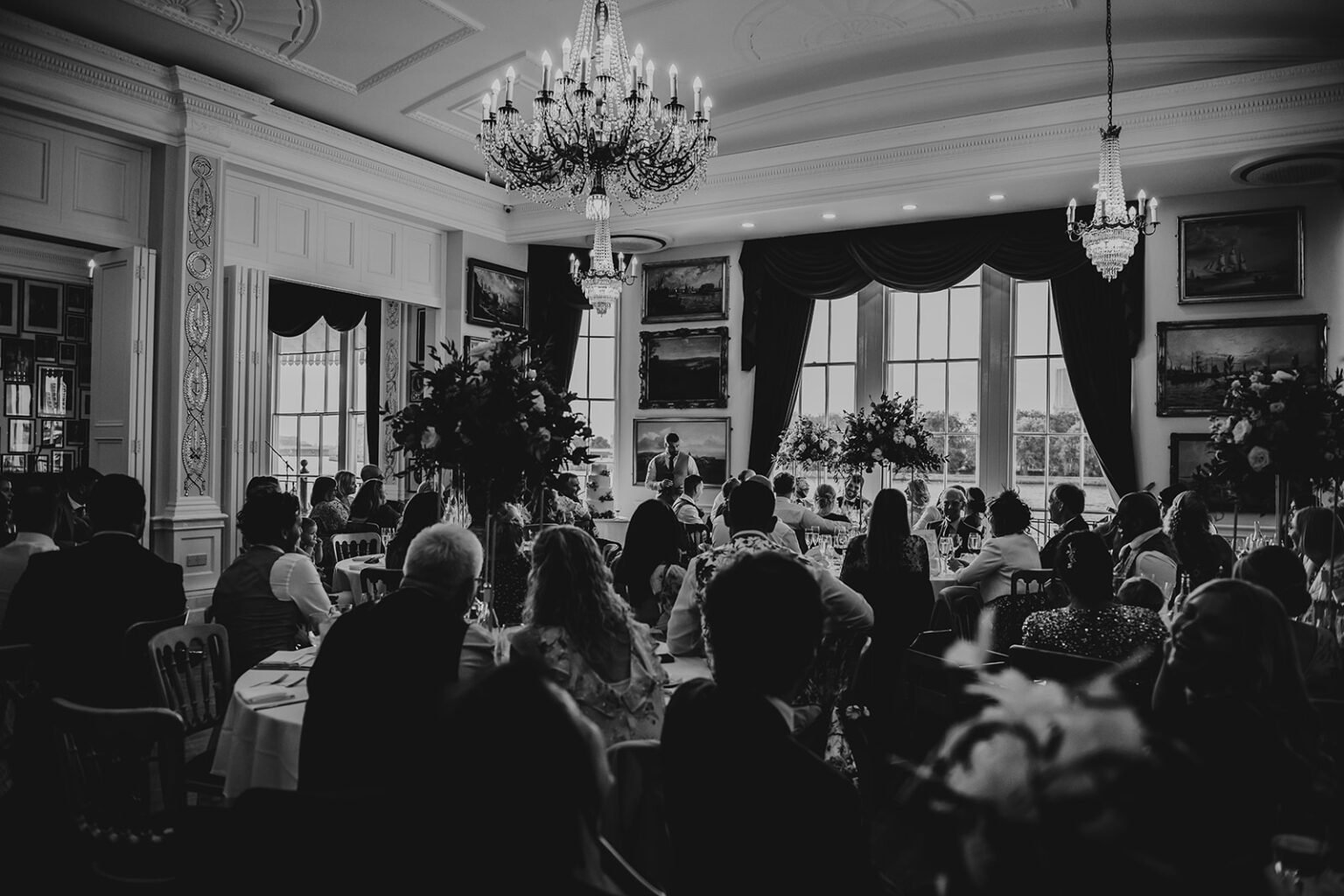 A best man giving a speech under luxury chandeliers in front of wedding guests at the Trafalgar Tavern wedding venue in London