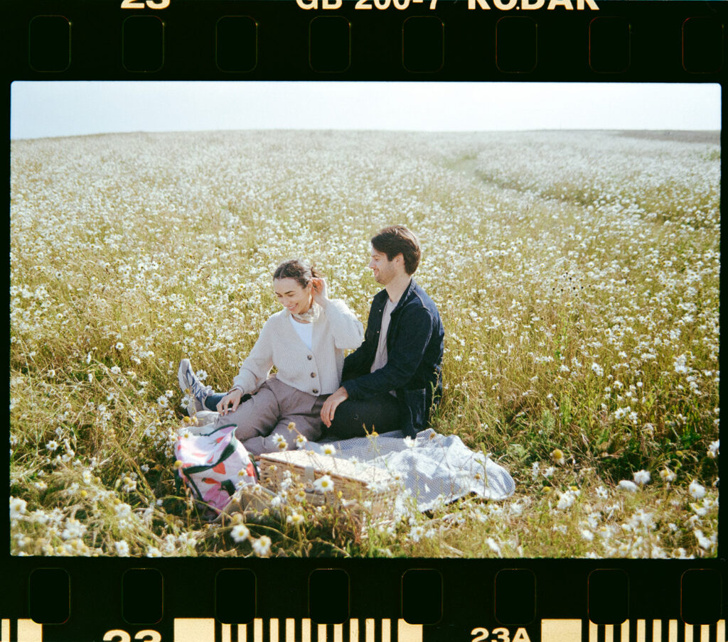 35mm film scan of a couple sat on blanket in a field with picnic basket