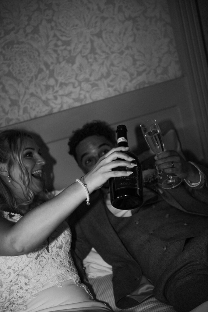 Direct flash portrait of bride and groom toasting champagne in bed
