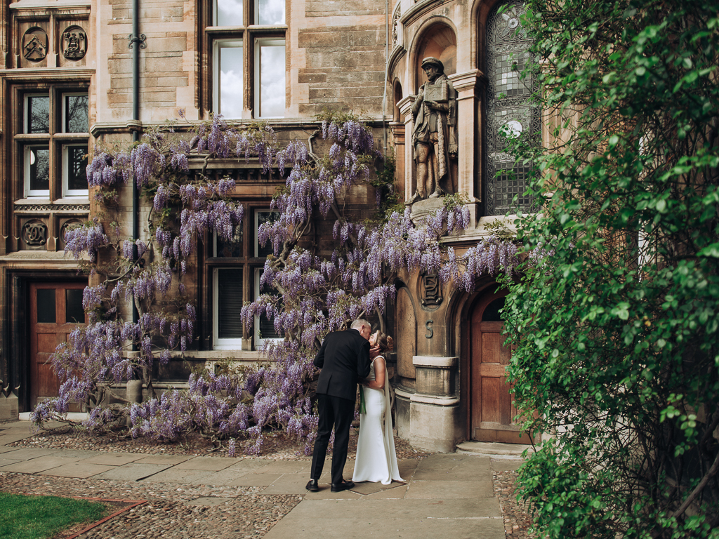 Bride and groom kissing by wysteria in gonville & caius college