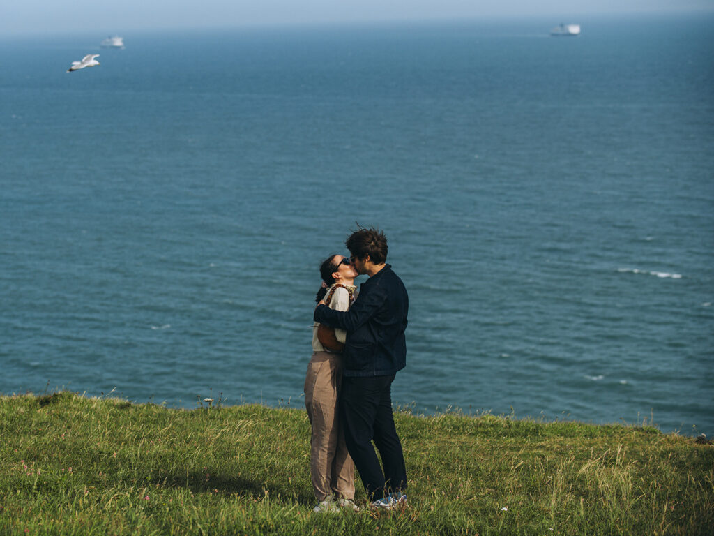 Newly engaged couple kissing with seagulls and ferries in the background