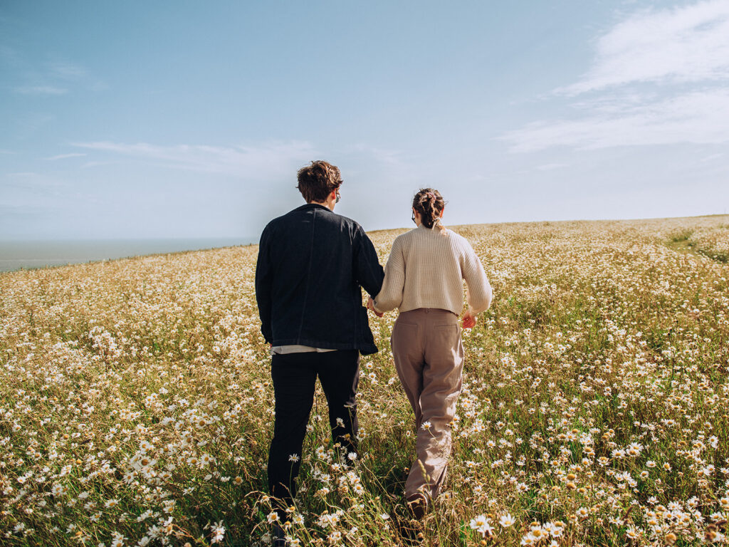 Newly engaged couple walking through daisy field