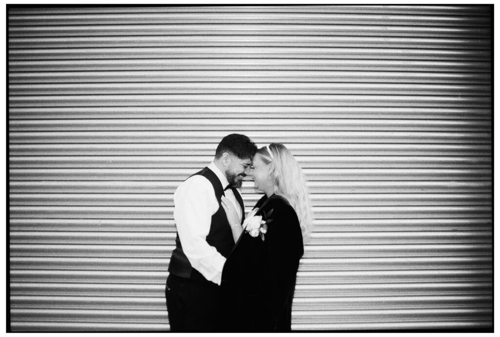 Bride and groom cuddling outside roller doors at wedding