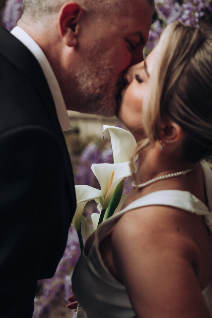 bride and groom kissing beside wysteria
