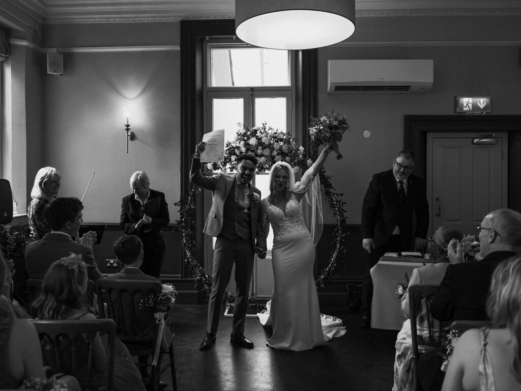 Bride and groom holding wedding certificate in the air