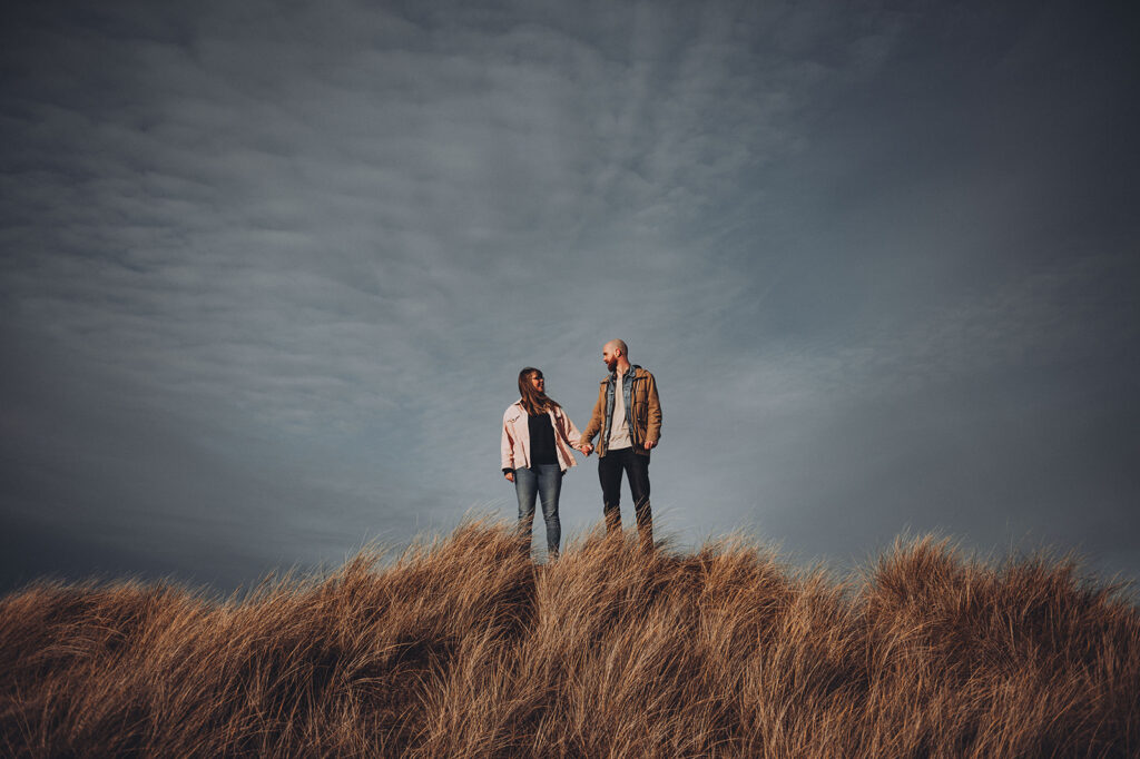 Couple standing at the top of a sand dune in Norfolk