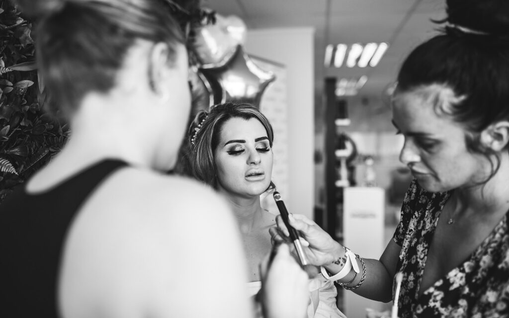 Bride having her hair and make-up being applied in a monochrome photograph for her summer wedding in Sandwich, Kent