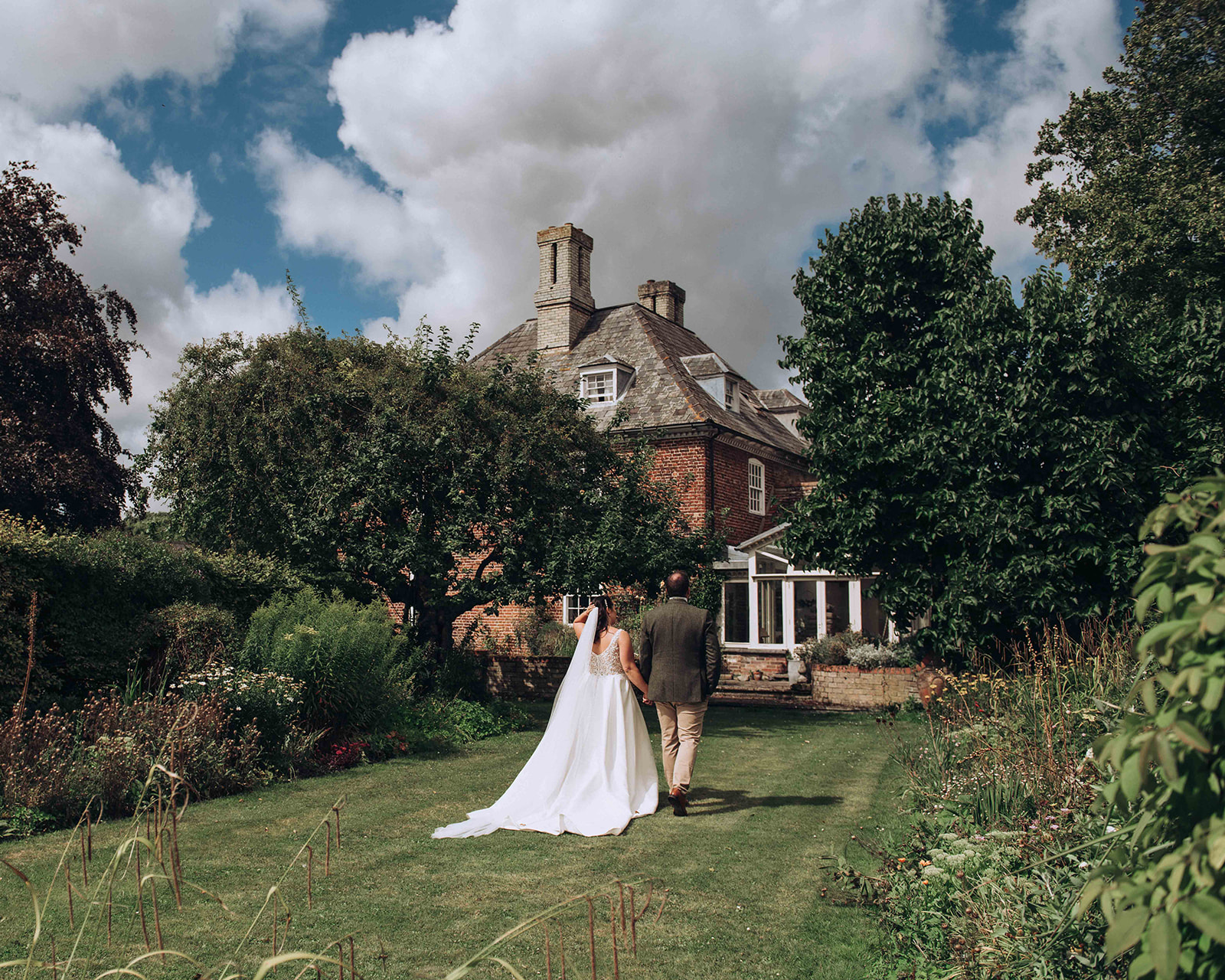 A couple walking in the manor garden of their luxury wedding in Kent.