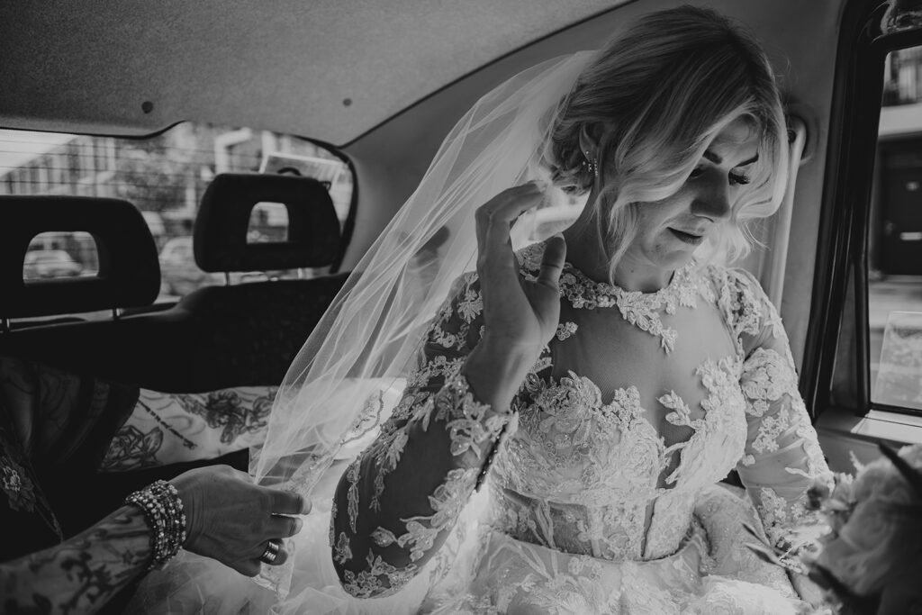 Editorial wedding shot of a bride in a taxi in black and white, her nails have been professionally done, not a traditional photo