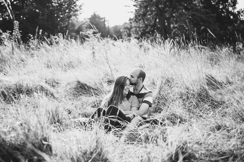 Couple sitting in a grassy field, sharing a tender moment during their engagement photoshoot.