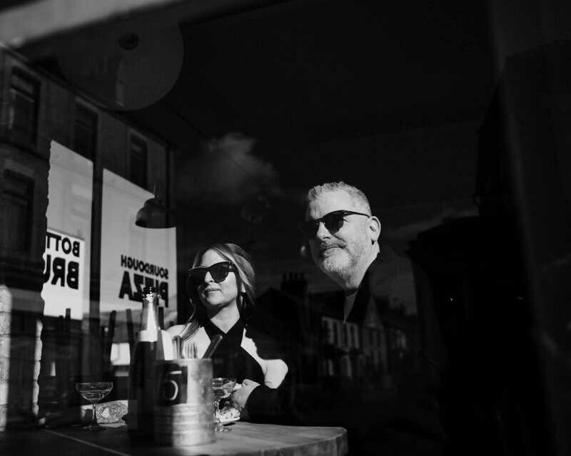 Stylish couple enjoying a drink at a bar, captured through the window