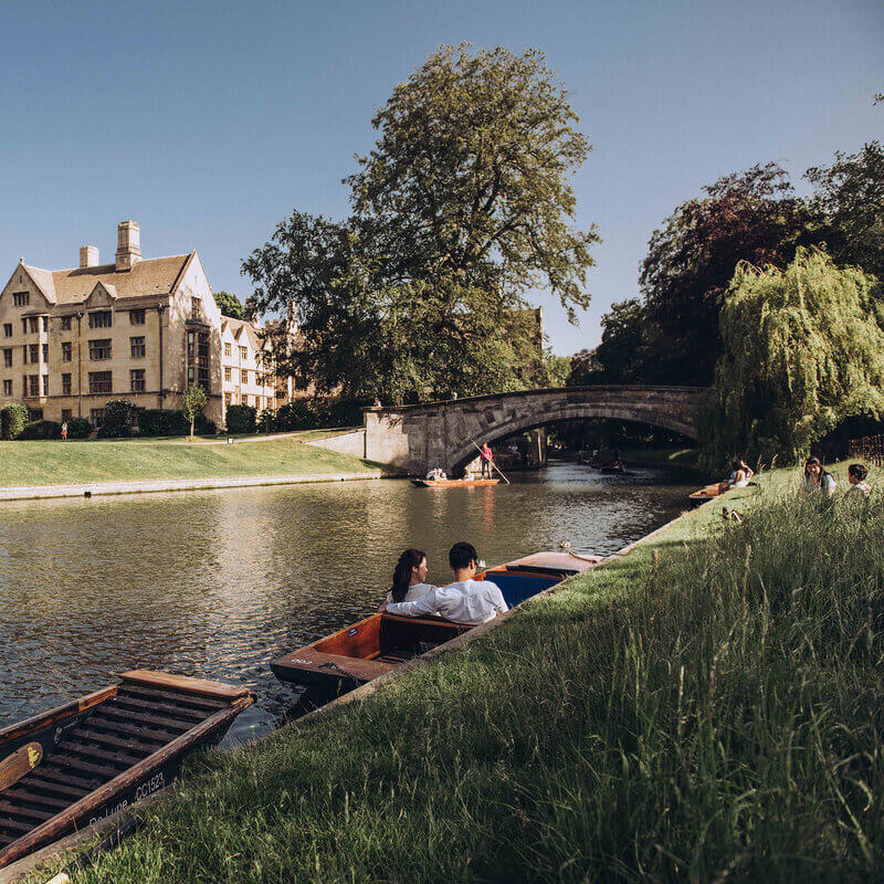 Couple enjoying a romantic boat ride along a scenic river, with historic architecture and a stone bridge in the background.