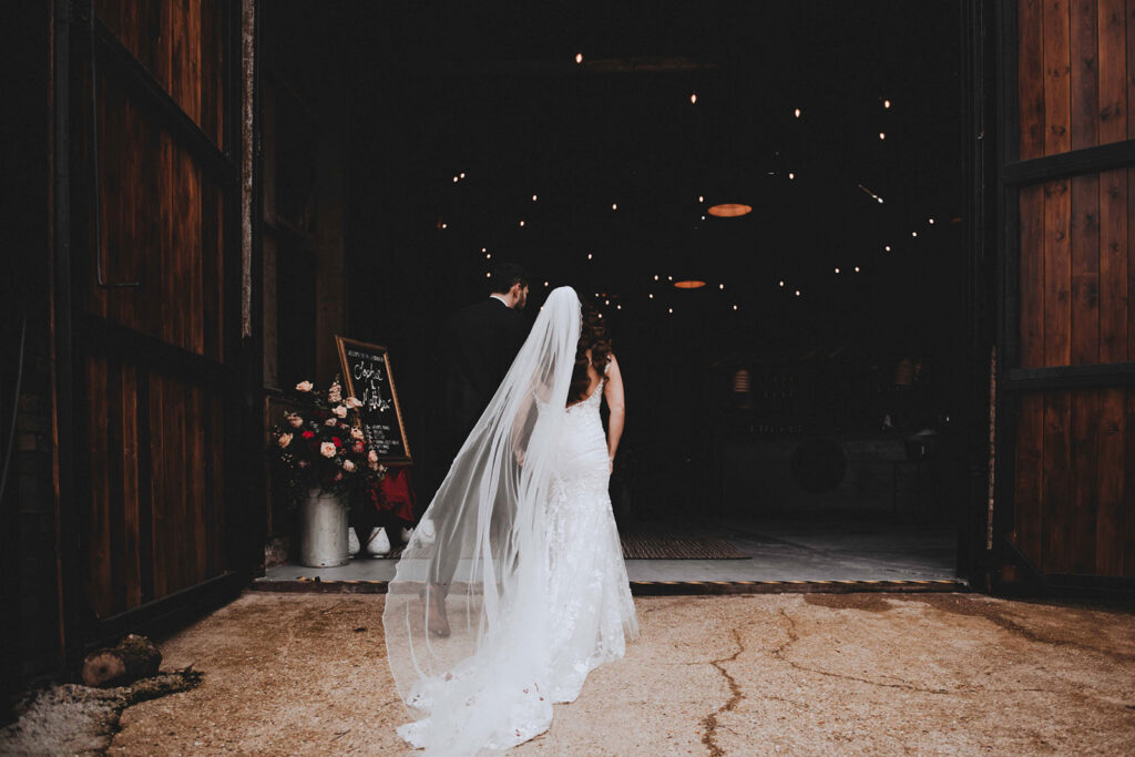 Bride with a long veil and groom walking into their wedding venue