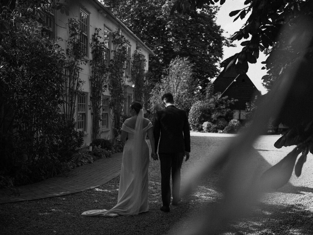 A photograph of a couple walking around the outside of the front of their wedding venue, behind the scenes of Editorial Wedding Photography: A Luxury Couple's Shoot in monochrome