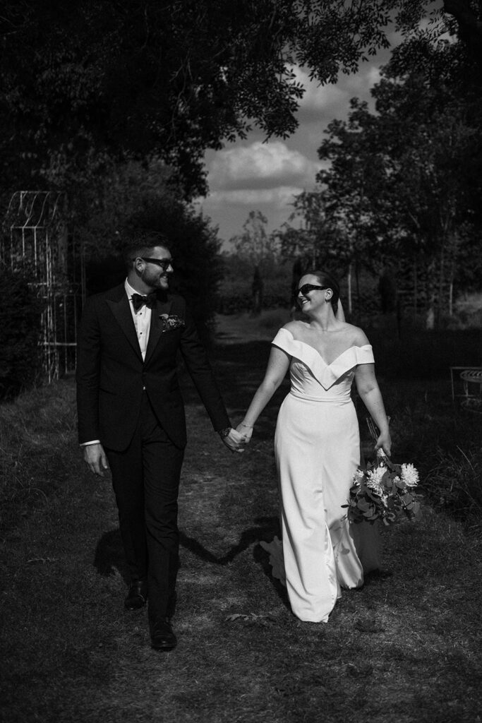 A couple walking hand in hand wearing sunglasses at their luxury wedding venue, behind the scenes of Editorial Wedding Photography: A Luxury Couple's Shoot in black and white