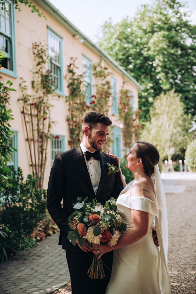 A photograph of a couple embracing outside of the front of their wedding venue, behind the scenes of Editorial Wedding Photography: A Luxury Couple's Shoot in monochrome