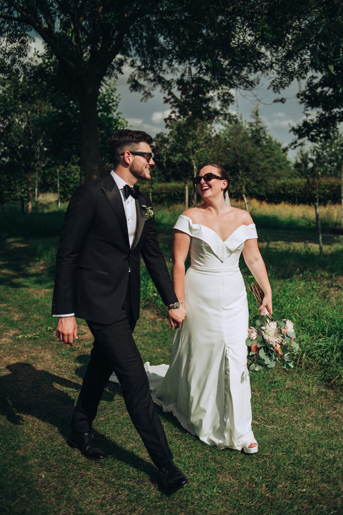 A couple laughing and walking hand in hand wearing sunglasses at their luxury wedding venue, behind the scenes of Editorial Wedding Photography: A Luxury Couple's Shoot