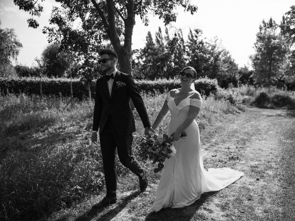 A couple strolling hand in hand wearing sunglasses at their luxury wedding venue, behind the scenes of Editorial Wedding Photography: A Luxury Couple's Shoot