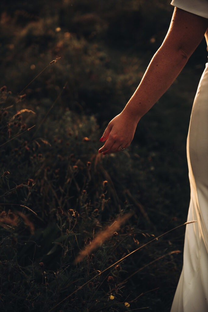 The hand of a bride walking beside wildflowers during sunset at their luxury wedding venue