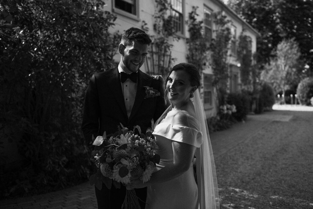 A photograph of a couple stood outside of the front of their wedding venue, behind the scenes of Editorial Wedding Photography: A Luxury Couple's Shoot in monochrome