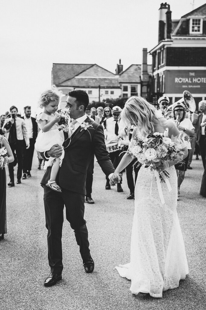 Newlywed couple cuddling their daughter walking across the prom on the beach in Deal Kent